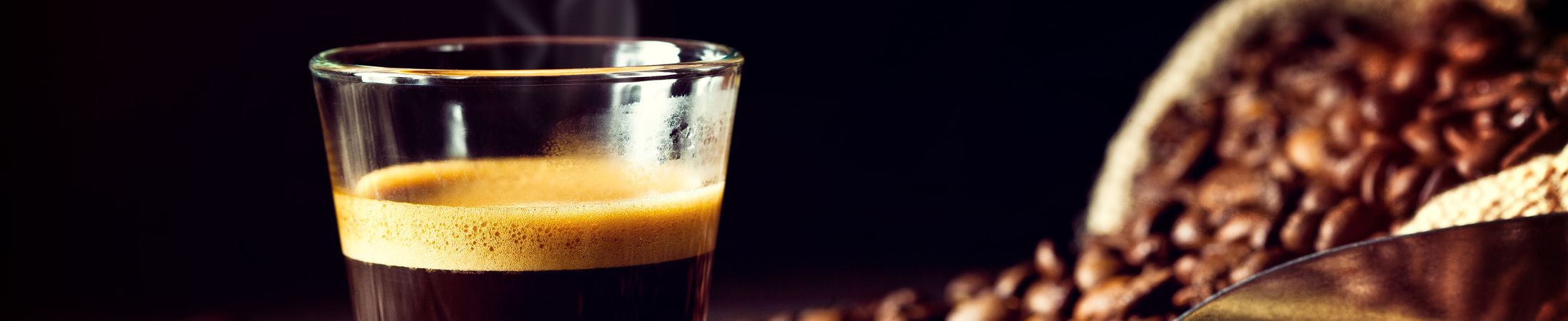 Frischer Espresso im Glas mit Kaffeebohnen drumherum