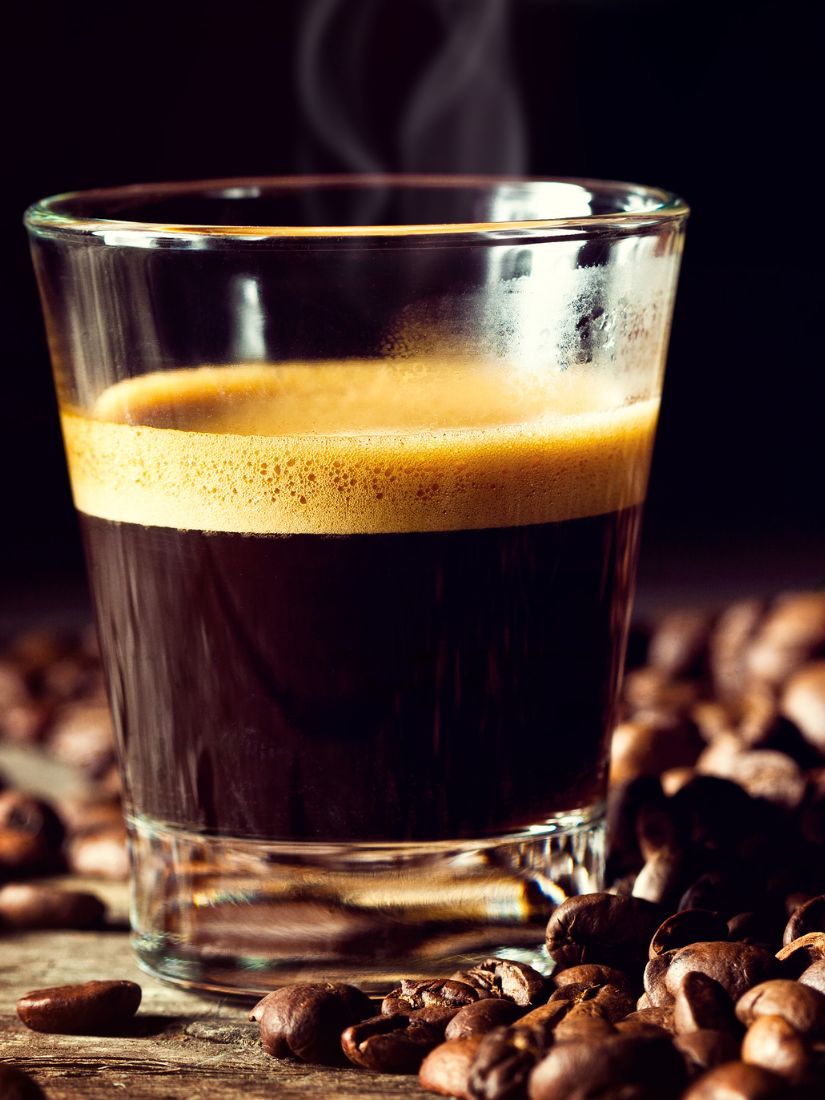 Frischer Espresso im Glas mit Kaffeebohnen drumherum